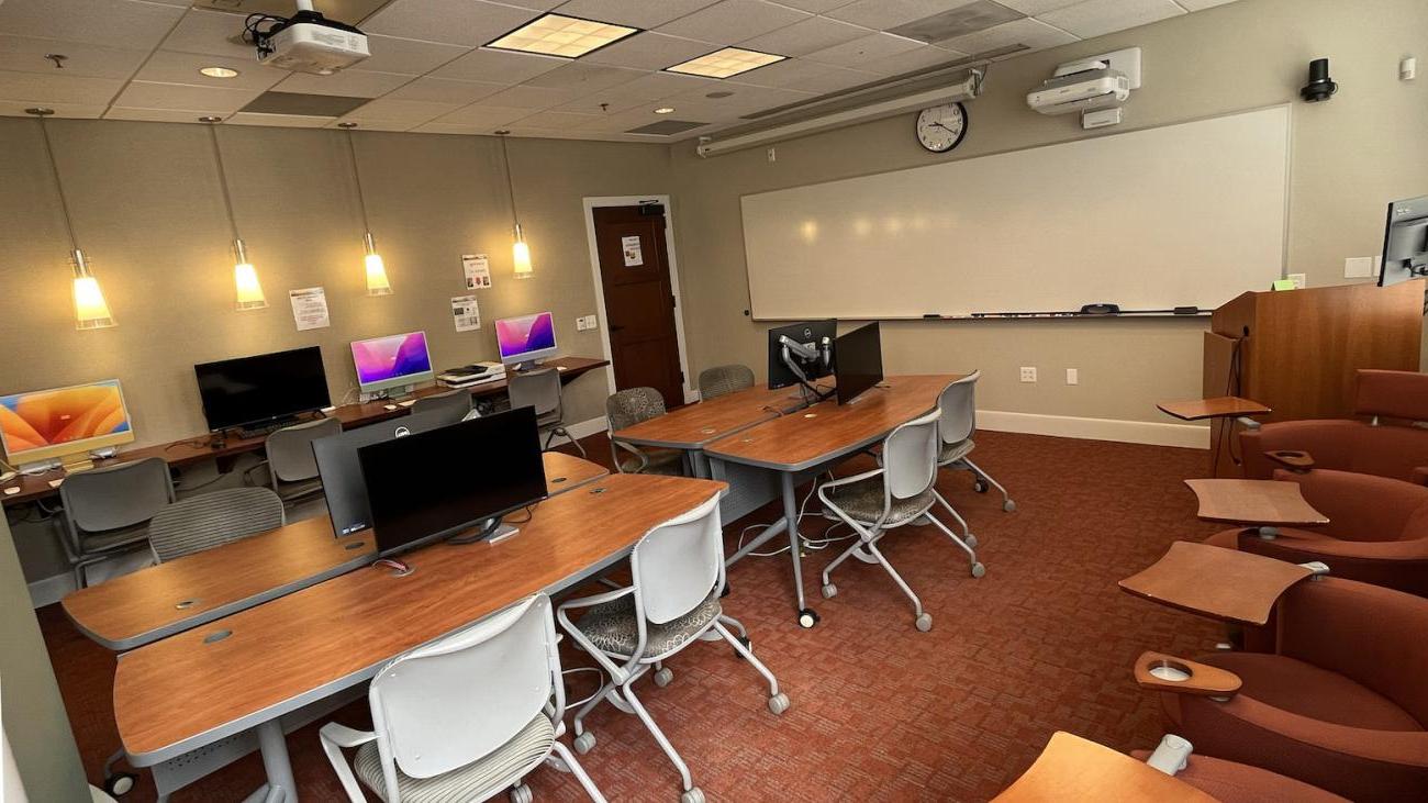 Classroom and lab section of the FLRC showing 27inch monitors, tables chairs, and imacs along the back wall.